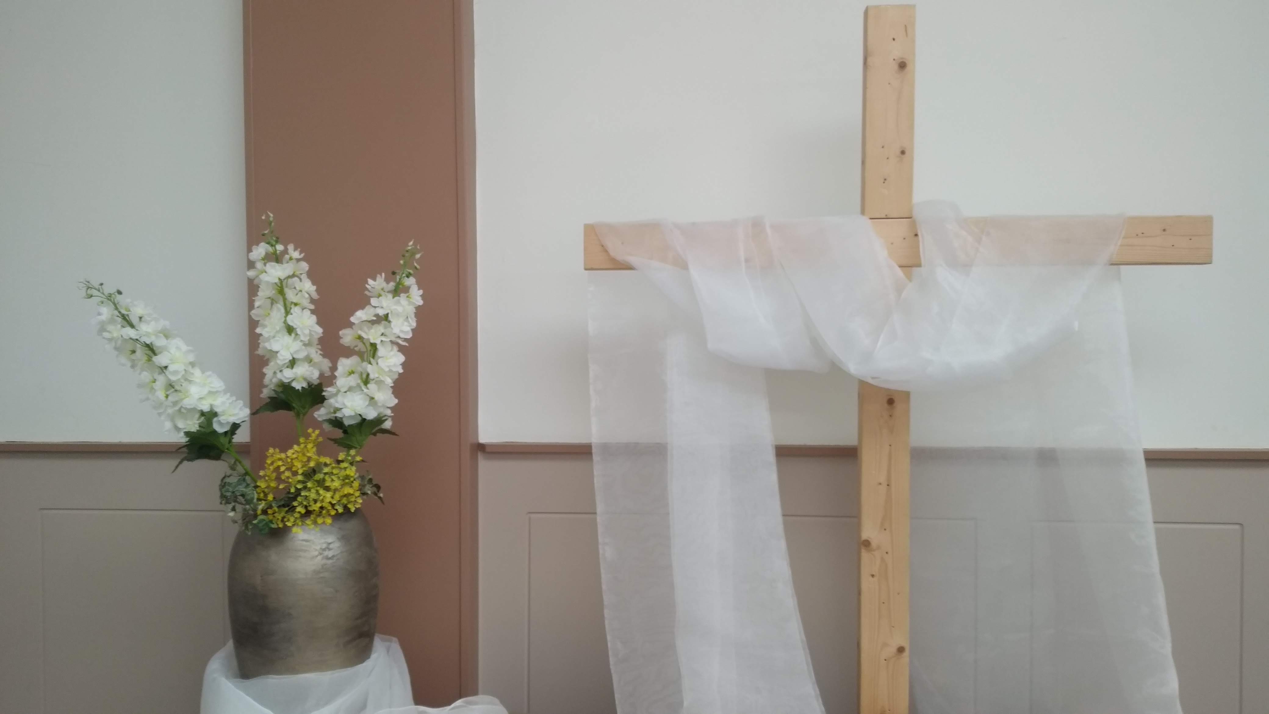 Een houten kruis met een witte doek, met bloemen ernaast