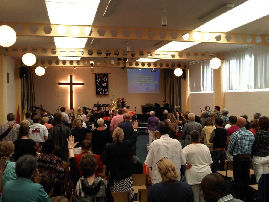 De samenkomstzaal van Ichthus tijdens de zondagse dienst, met de gemeente staand in aanbidding